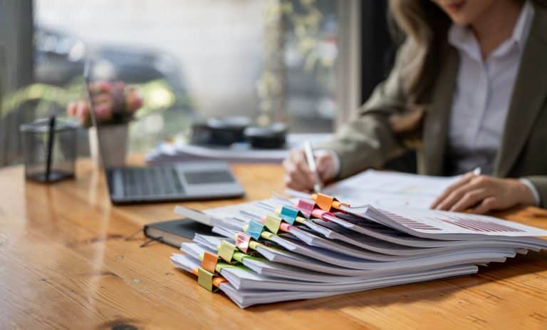 pile of documents and hand out of focus in background Big Changes Coming for Non-Compete Agreements: Is Your Business Ready?